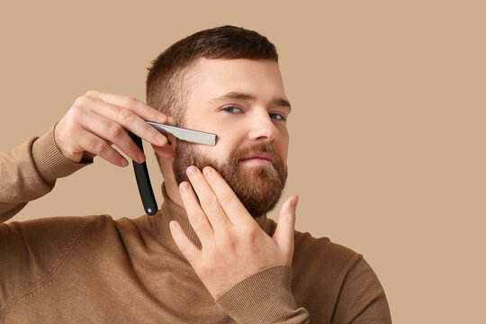 Young bearded man with open razor on color background