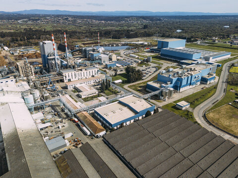 Aerial view of a sprawling industrial plant with towering white and red chimneys and vast blue-roofed structures, bordered by green, Cacia, Aveiro District, Portugal.