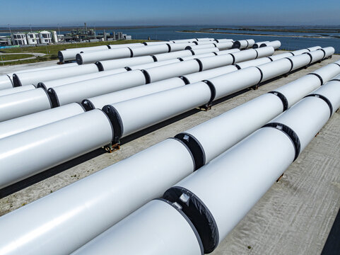 Aerial view of rows of bright white pipes stretch across the frame under the vast sky, contrasting with the dark water, Aveiro, Aveiro, Portugal.