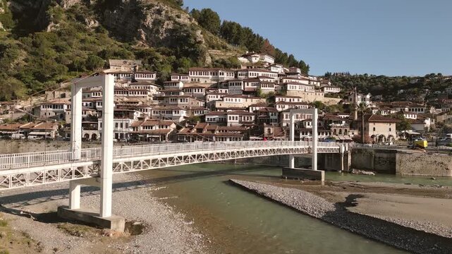 Aerial panning view Berat - A city of a thousand windows. Gorica Bridge crossing Osum river with Mangalem quarter Ottoman houses hillside UNESCO town Balkan travel destination in Albania