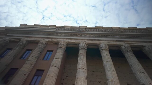 Ancient Corinthian columns of the Temple of Hadrian against a cloudy blue sky in Piazza di Pietra, Rome, a famous UNESCO world heritage site and popular european tourist destination in Italy