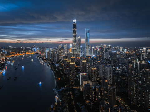 Aerial view of golden lights reflecting on the river against the backdrop of skyscrapers under a twilight sky, Shanghai, China.