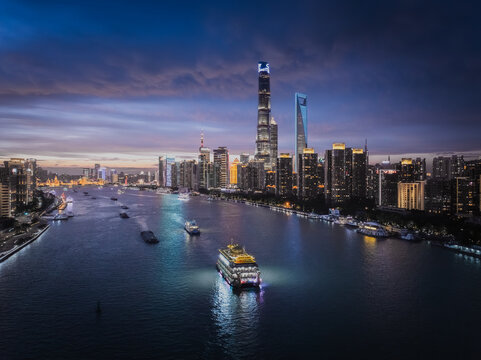 Aerial view of the gleaming Huangpu River reflecting the city lights under a twilight sky, with boats gliding past the illuminated skyscrapers, Shanghai, China.