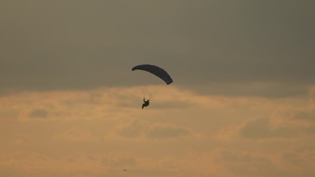 Paraglider sunset silhouette soaring through a golden evening sky over the calm sea horizon at twilight