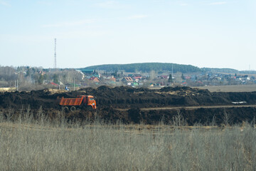 Fototapeta premium Construction Site with an Orange Dump Truck Working on Earth Moving and Land Preparation for Future Development in a Rural Landscape