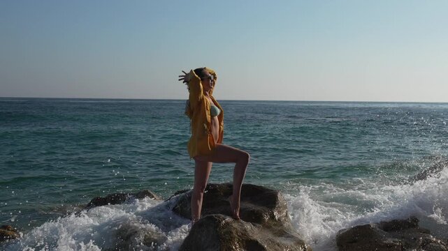 Woman beach rocks attractive female model in a yellow shirt posing on a large rock with waves splashing on a sunny day