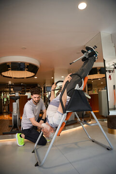 Older man on inversion table assisted by younger male indoors