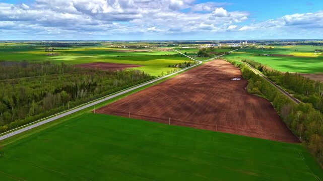 Farmland patches divided by a road under a cloudy sky on a spring day in aerial view