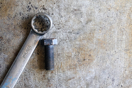 A ring wrench tool lying next to a steel bolt on a weathered and scratched industrial metallic background. Copy text