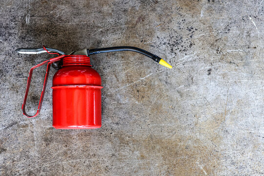 A classic red manual pump oiler can placed on a weathered and scratched metallic industrial background.
