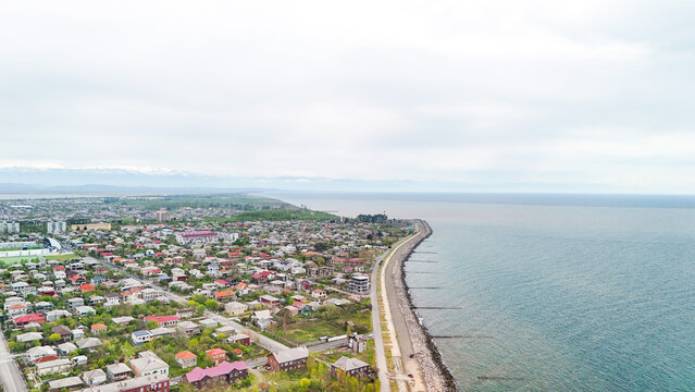 Poti, georgia cityscape drone view showing the black sea coast with a long breakwater, residential buildings, and distant snow capped mountains under a cloudy sky