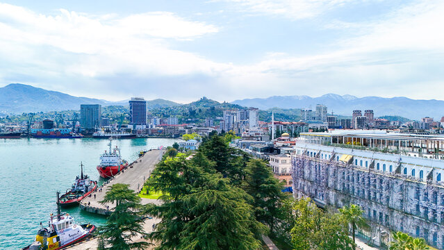 Batumi cityscape, georgia, showing the black sea port and harbor with ships docked at the pier, modern high rise buildings, and the caucasus mountains in the background