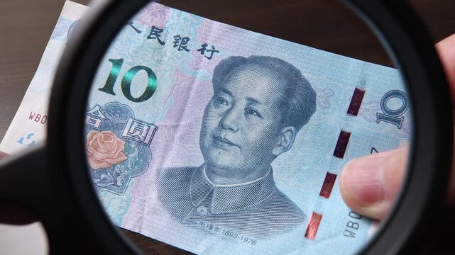 Examination of 10 Chinese Yuan (CNY) cash money with magnfication glass, loupe. Concept of authenticity check, fight against counterfeiting of banknotes, anti fraud measures in China. Close up view.