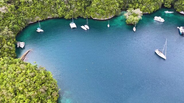 Aerial view of a secluded cove surrounded by lush green islands with boats anchored in turquoise waters.
