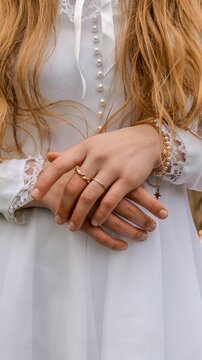 Close-up of a young girl's hands in a white dress with pearl buttons and lace trim