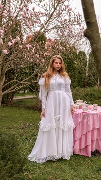 Young woman in a white vintage dress posing near a blooming magnolia tree