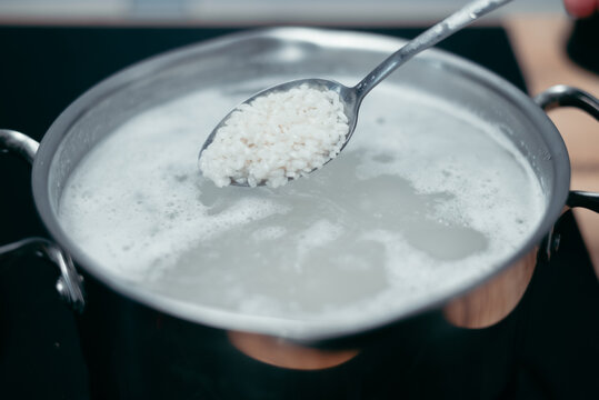 A spoon is holding rice above a pot filled with boiling water on a stove. This scene depicts the process of cooking rice, which is a common staple in many meals around the world