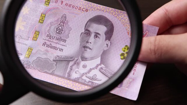 Examination of 500 Thai baht (THB) cash money with magnfication glass, loupe. Concept of authenticity check, fight against counterfeiting of banknotes, anti fraud measures in Thailand. Close up view.