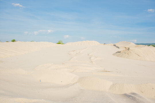 View of large sand dunes and industrial piles with tire tracks under a clear blue sky in Futog, Vojvodina, Serbia.