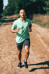 Obraz premium Male runner jogging on rural dirt road in forest during daytime