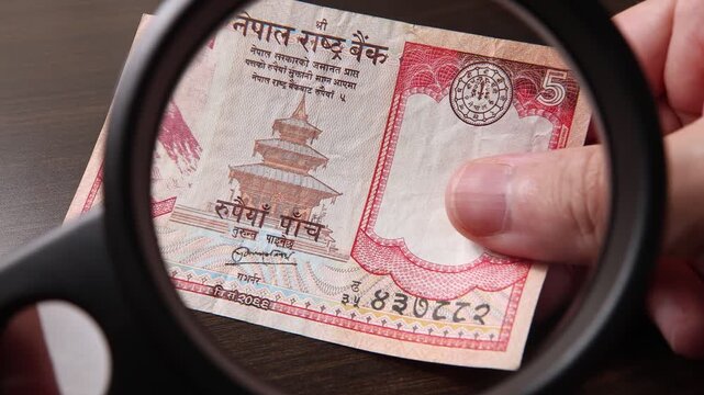 Examination of 5 Nepalese rupee (NPR) cash money with magnfication glass, loupe. Concept of authenticity check, fight against counterfeiting of banknotes, anti fraud measures in Nepal. Close up view.