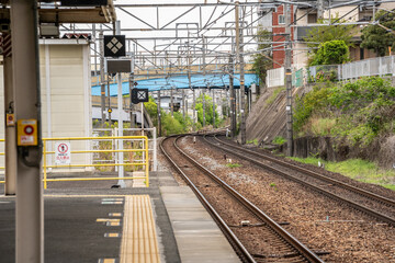 Fototapeta premium Curving railway tracks at a suburban train station in Japan with overhead power lines and modern residential architecture.