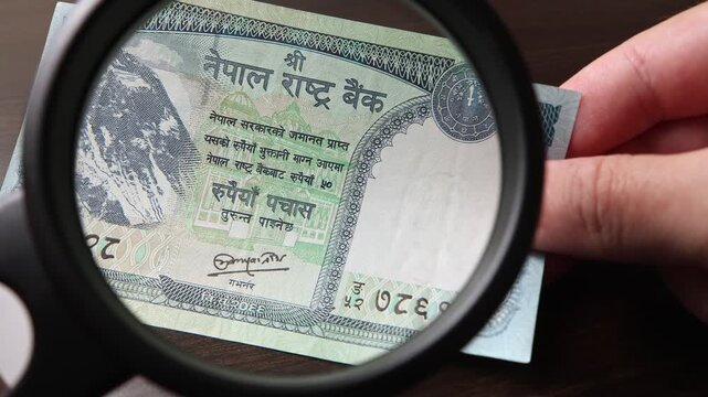 Examination of 50 Nepalese rupee (NPR) cash money with magnfication glass, loupe. Concept of authenticity check, fight against counterfeiting of banknotes, anti fraud measures in Nepal. Close up view.