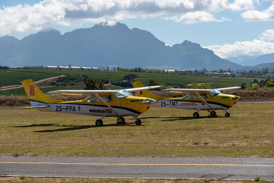 Stellenbosch Western Cape Soutsh Africa.  10.02.2026. Two small yellow aircraft parked side-by-side on a dry grassy field, with Simonsberg mountain  and vineyards visible behind them. 