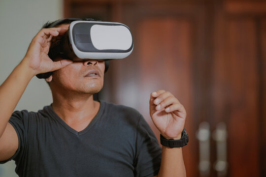 Asian man looking at vr box, virtual reality glasses at home. People and technology metaverse concept, viewing 360 videos.