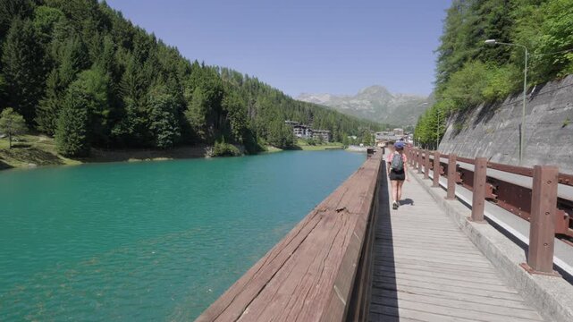 Back View Of Woman Walking On Wooden Pathway Along Diga di Madesimo In Lombardy, Italy. wide shot