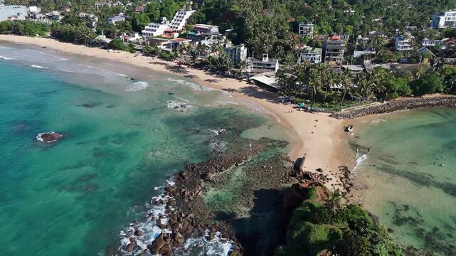 View of the turquoise ocean water surrounding Parrot Rock and the sandy coast. Mirissa, Sri Lanka