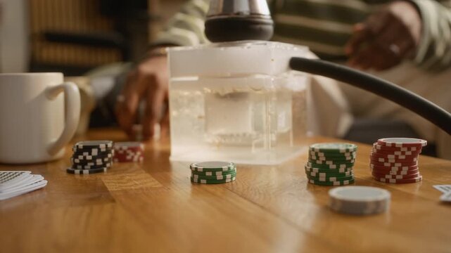 Close up of unrecognizable friends making bet, using chips, while playing poker and smoking hookah during party at home