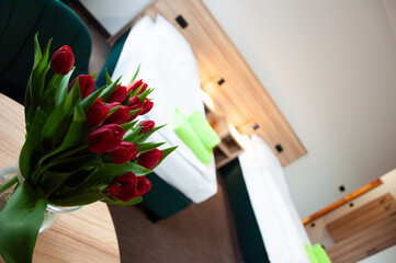 Bukiet czerwonych tulipanów ustawiony w pokoju hotelowym. Dekoracyjne kwiaty ocieplają wnętrze i podkreślają przytulny, elegancki charakter miejsca noclegowego. © Freshfanpage