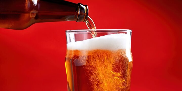 Amber beer with frothy head being poured into a clear glass on a red background