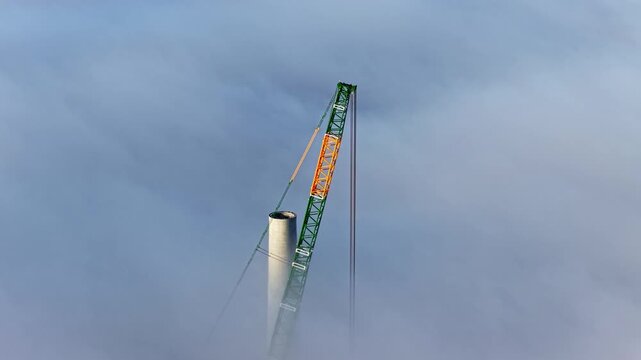 Green and orange crane tip piercing through a soft layer of low-lying clouds