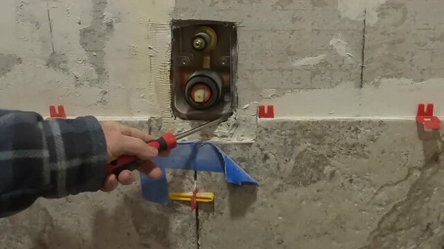 Women chiseling tile around shower diverter 2