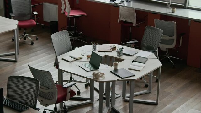 High angle view of modern comfortable coworking space featuring modular desks surrounded by ergonomic chairs and equipped with laptops and stationery