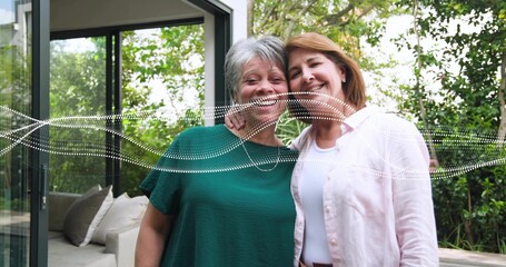 Naklejka premium Smiling mom and daughter posing on patio by sliding door, green, pink tops, white dotted overlay