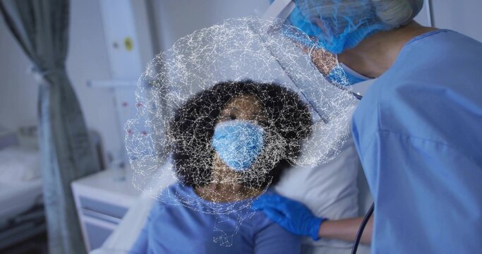Examining clinician in blue scrubs checking masked patient on bed, gown, stethoscope, overlay
