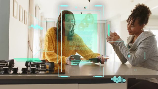 Woman in yellow picking phone, passing and showing friend in kitchen, tech HUD on screen, laughing