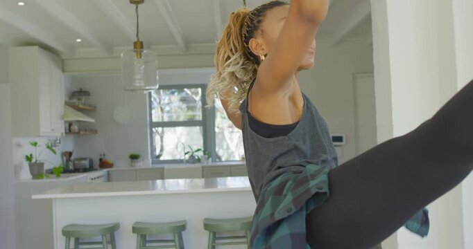 African American woman turning, sweeping arm, lifting leg into high kick at kitchen island training