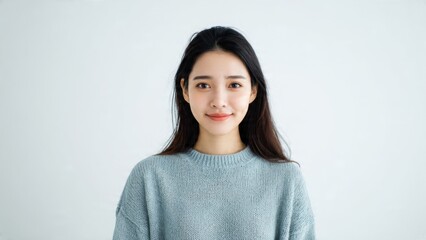 Fototapeta premium Natural headshot portrait of a beautiful young Asian woman with a happy, authentic smile, wearing a casual blue knitted sweater against a clean white background, exuding genuine contentment.