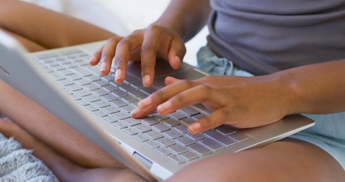 Female placing hands on keyboard, typing on silver laptop on bed in tank and shorts working