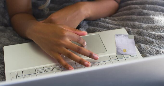 Female in tank top tapping laptop trackpad on bed, reaching for chip card, inspecting details