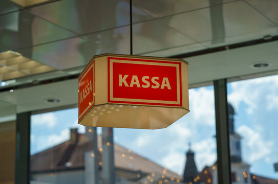 Close-up of red cash register sign reading Kassa inside modern shop, with blurred city view in background, retail concept and payment area detail