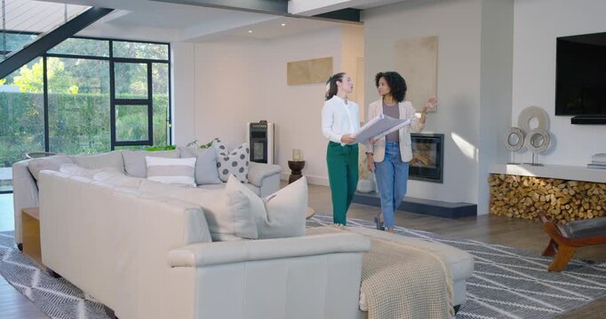 Diverse women entering living room, walking, scanning window and beam, unrolling plans for design