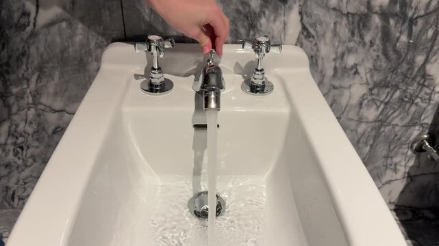 Hand pulling up sink stopper control on bathroom faucet, close up