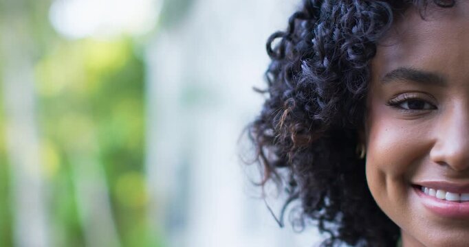 Camera pulling back as woman smiling, revealing dimples and earring by pale wall, copy space