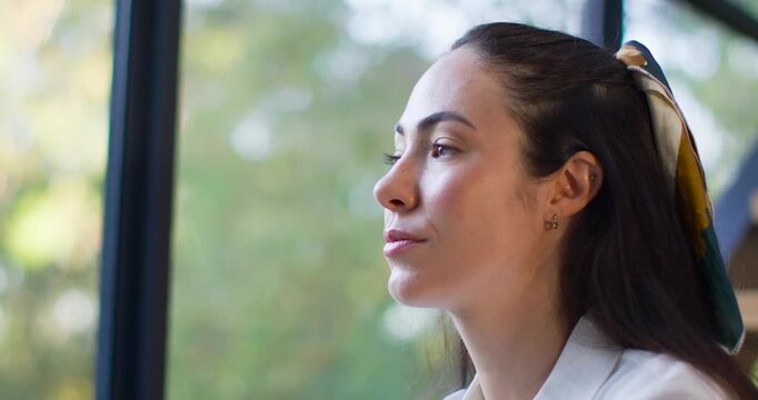 Woman sitting by large window, pausing then opening eyes, turning to camera making eye contact