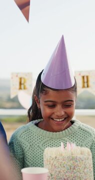 Birthday, happy and child with cake at party for celebration, special day and thinking of wish outdoor. Family, excited and girl with decorations, hat and candles for event, gathering and milestone